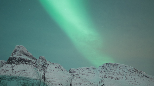 a green light in the sky over snowy mountains