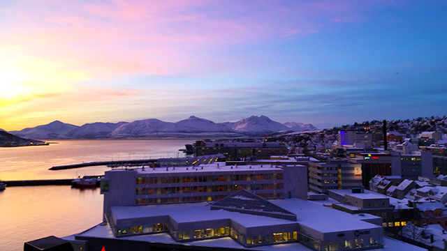 a building with snow on it and a body of water with mountains in the background