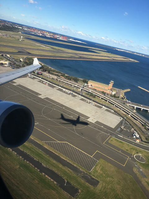 an airplane wing and runway with water and buildings in the background