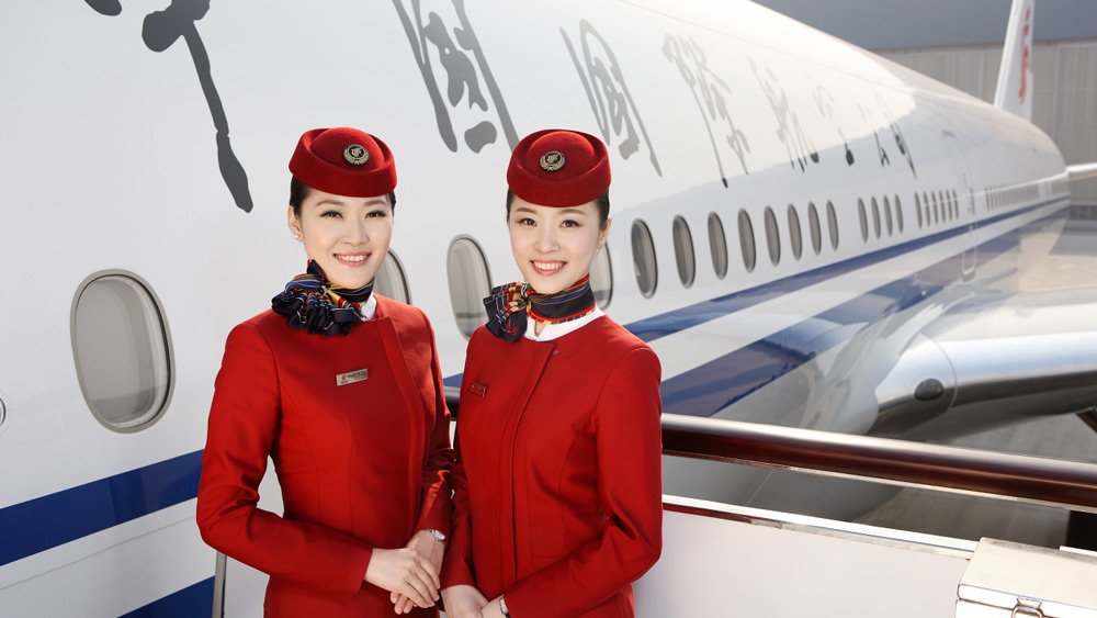 two women wearing red uniforms and hats standing in front of a plane