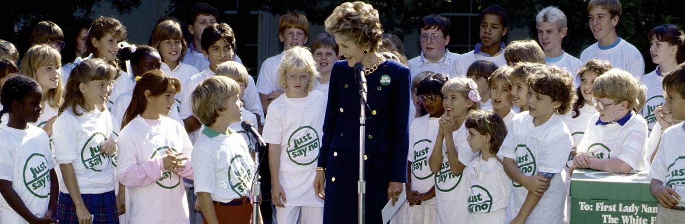 a woman speaking into a microphone with a group of children