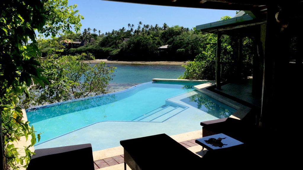 a pool with a deck and chairs on a deck overlooking a body of water