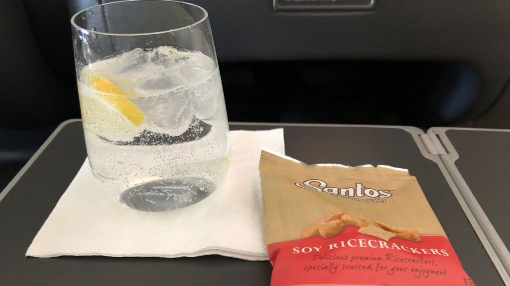 a glass of water with ice and lemon on a napkin next to a bag of rice crackers