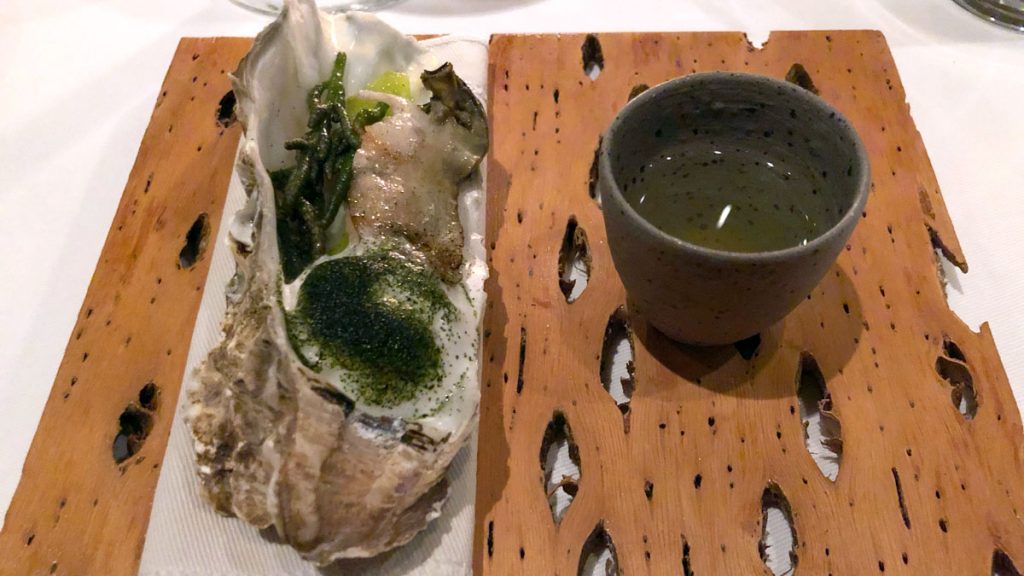 a oyster shell and a cup of liquid on a wooden tray
