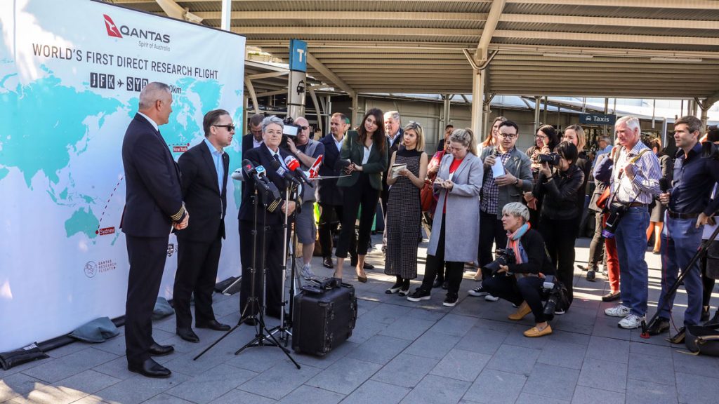 a group of people standing around a man speaking into microphones