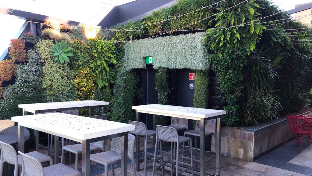 a white tables and chairs outside with plants on the wall