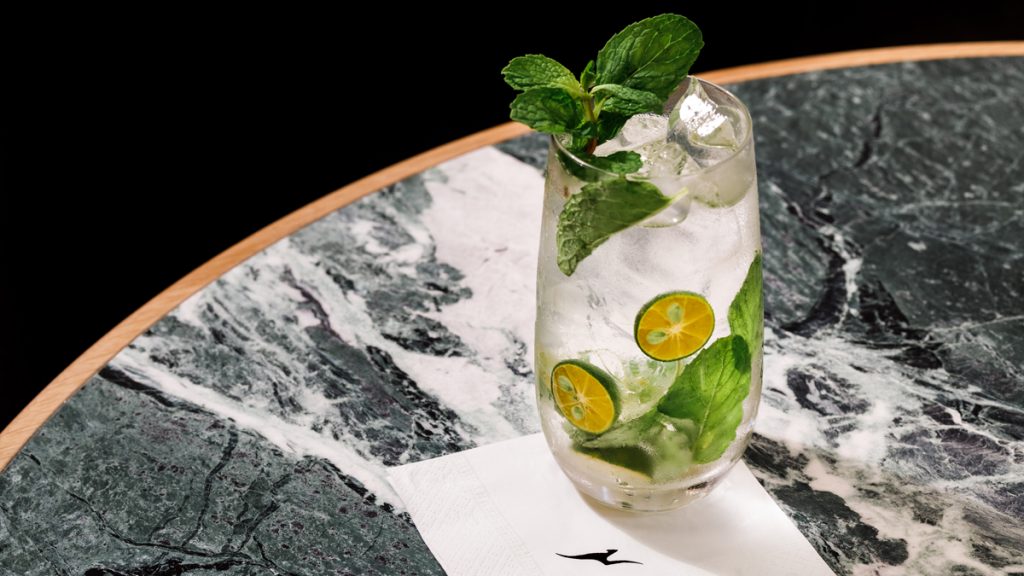 a glass of water with mint leaves and limes on a table
