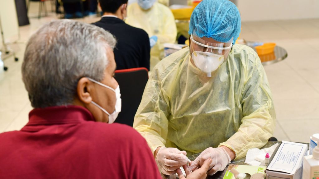 a man wearing a mask and gloves while another man in a mask is getting a manicure