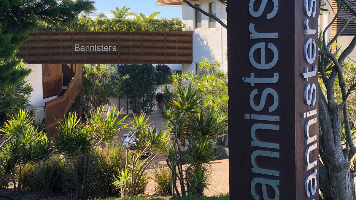 a sign with a white text and a white building with trees