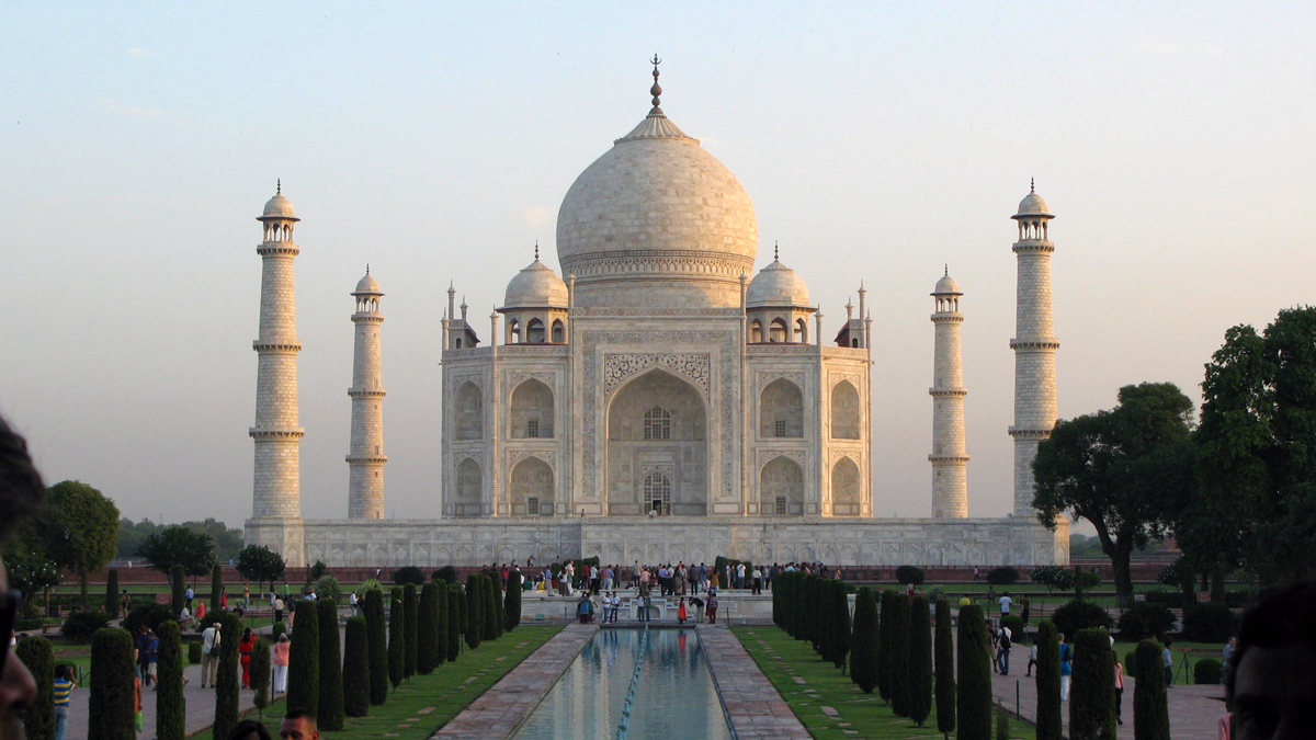 a large white building with towers and a pool of water with Taj Mahal in the background