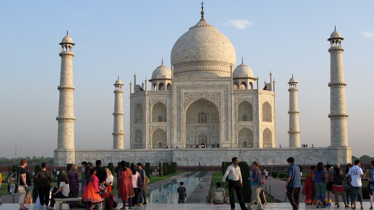 a group of people standing in front of a white building with Taj Mahal in the background