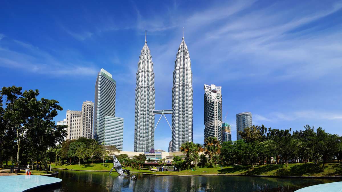 Petronas Towers skyline with a pond and trees