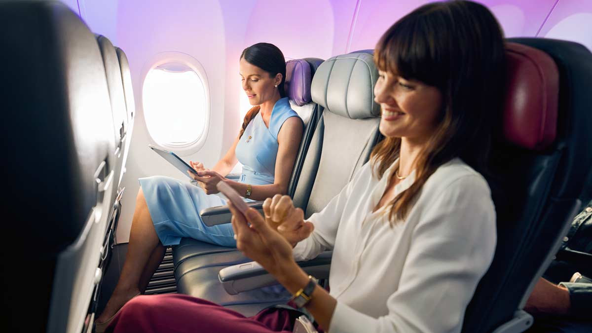 women sitting in an airplane with a tablet and a woman in the background